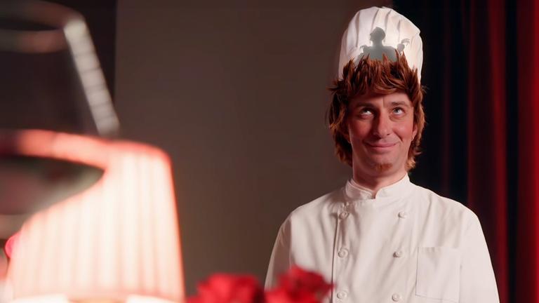 Jan Böhmermann trägt eine weiße Kochmütze, hinter der ein Schatten zu erkennen ist. Die Inszenierung nimmt Bezug auf den Animationsfilm "Ratatouille".