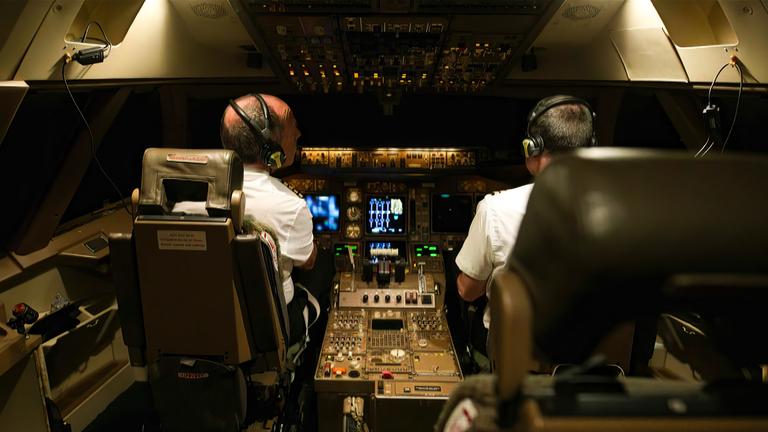Zwei Piloten sitzen im Cockpit, mit dem Rücken zur Kamera.