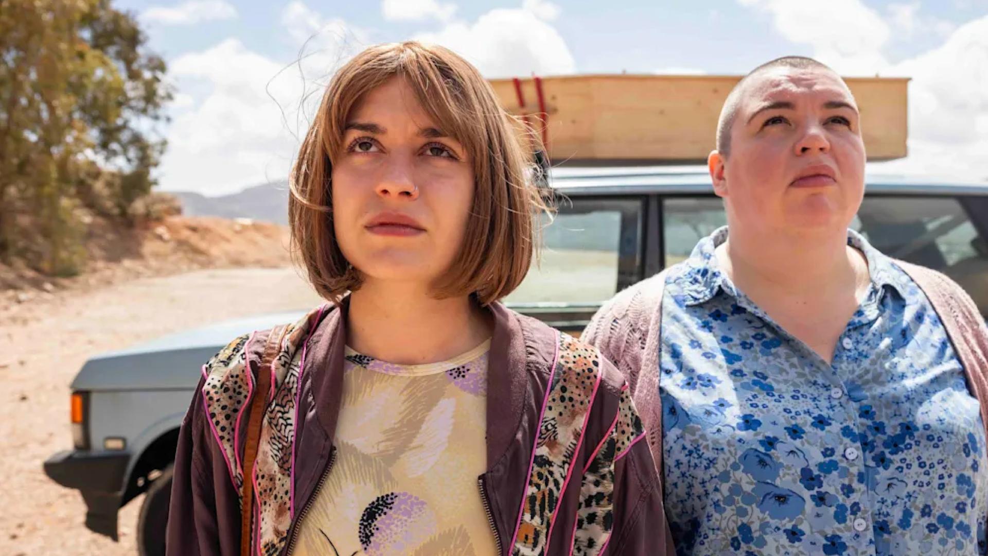 Anna und Kat stehen in Richtung der Kamera und haben ihren Blick in den Himmel gerichet. Im Hintergrund ist ein Auto zu sehen.