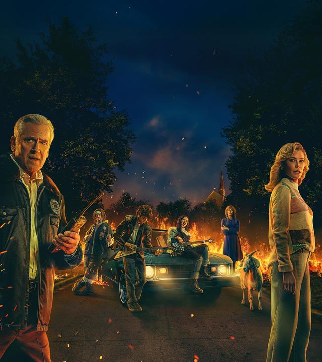 Im Vordergrund stehen ein Mann und eine Frau, die entsetzt in Richtung Kamera schauen. Im Hintergrund ist ein brennendes Auto zu sehen. Vor dem Auto sind zwei Jungs und ein Mädchen mit ihren Instrumenten zu sehen.