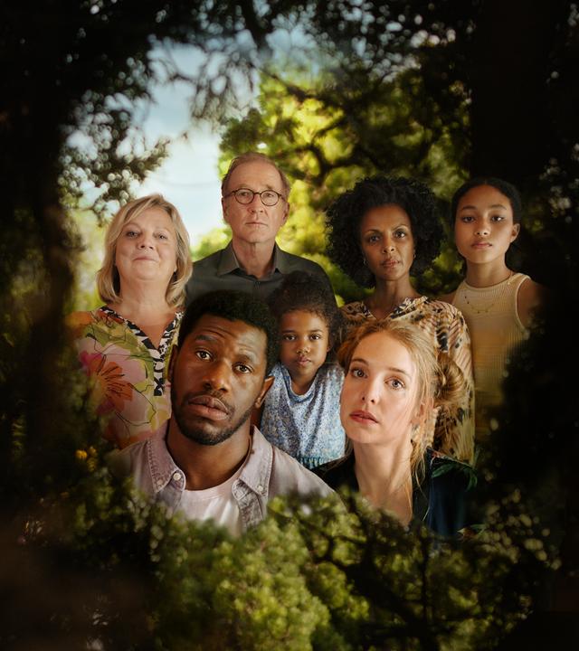 I don't work here: In einer grünen Hecke ist ein Loch, durch das man einen Blick hinter die Hecke werfen kann. Dort ist eine Gruppe von Menschen zu sehen: Ganz vorne die Köpfe von Dawit (Akeem van Flodrop, 2.v.l.) und Laura (Sina Martens, 3.v.r.). Hinter ihnen stehen Heidi (Gabriela Maria Schmeide, l.), Walter (Peter Lohmeyer, 3.v.l.), Fiyori (Lousia Heinricht, M.), Lemlem (Dennenesch Zoudé, 2.v.r.) und Armana (Chioma Chukwuani, r.).