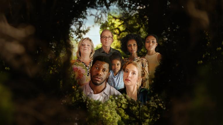 I don't work here: In einer grünen Hecke ist ein Loch, durch das man einen Blick hinter die Hecke werfen kann. Dort ist eine Gruppe von Menschen zu sehen: Ganz vorne die Köpfe von Dawit (Akeem van Flodrop, 2.v.l.) und Laura (Sina Martens, 3.v.r.). Hinter ihnen stehen Heidi (Gabriela Maria Schmeide, l.), Walter (Peter Lohmeyer, 3.v.l.), Fiyori (Lousia Heinricht, M.), Lemlem (Dennenesch Zoudé, 2.v.r.) und Armana (Chioma Chukwuani, r.).