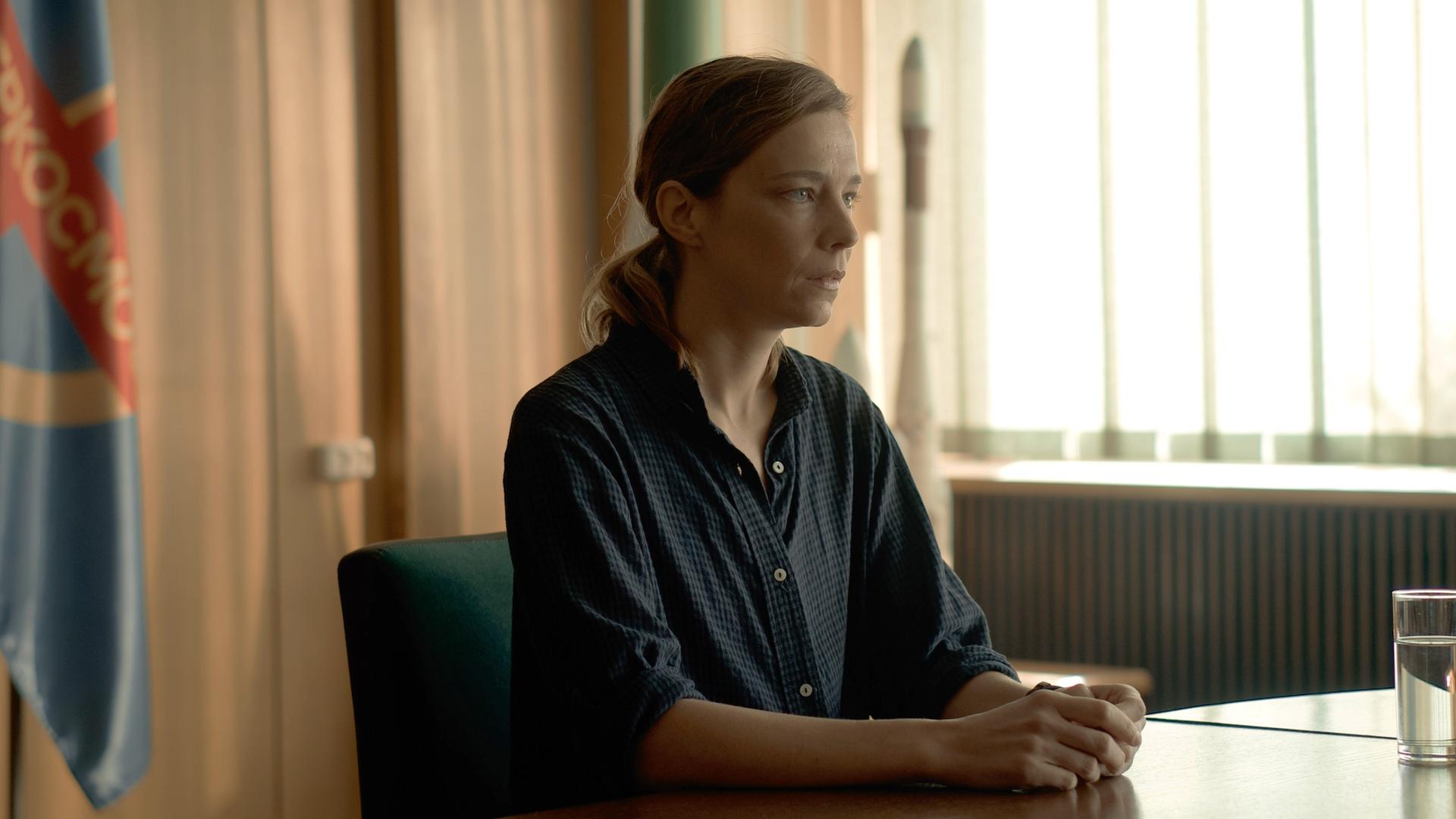 Anna Zarathi (Céline Sallette) sitzt in einem Konferenzsaal und schaut konzentriert in die Ferne.