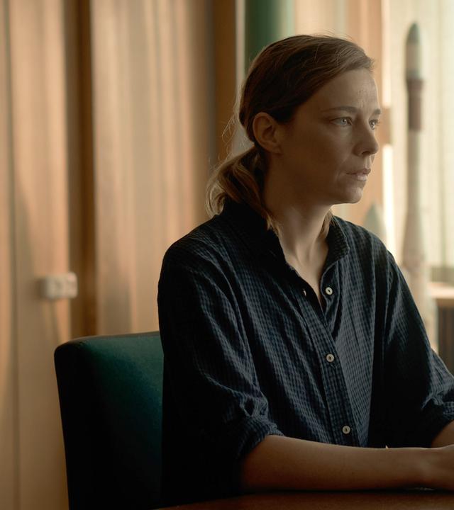 Anna Zarathi (Céline Sallette) sitzt in einem Konferenzsaal und schaut konzentriert in die Ferne.