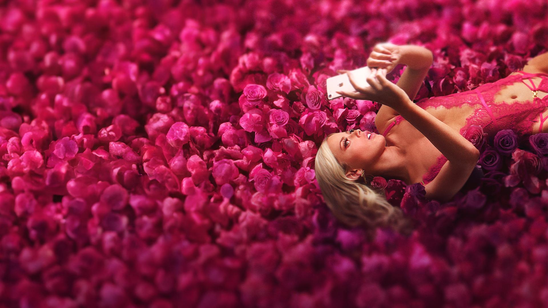 Selina liegt mit ihrem Smartphone in der Hand auf einem Rosenfeld.