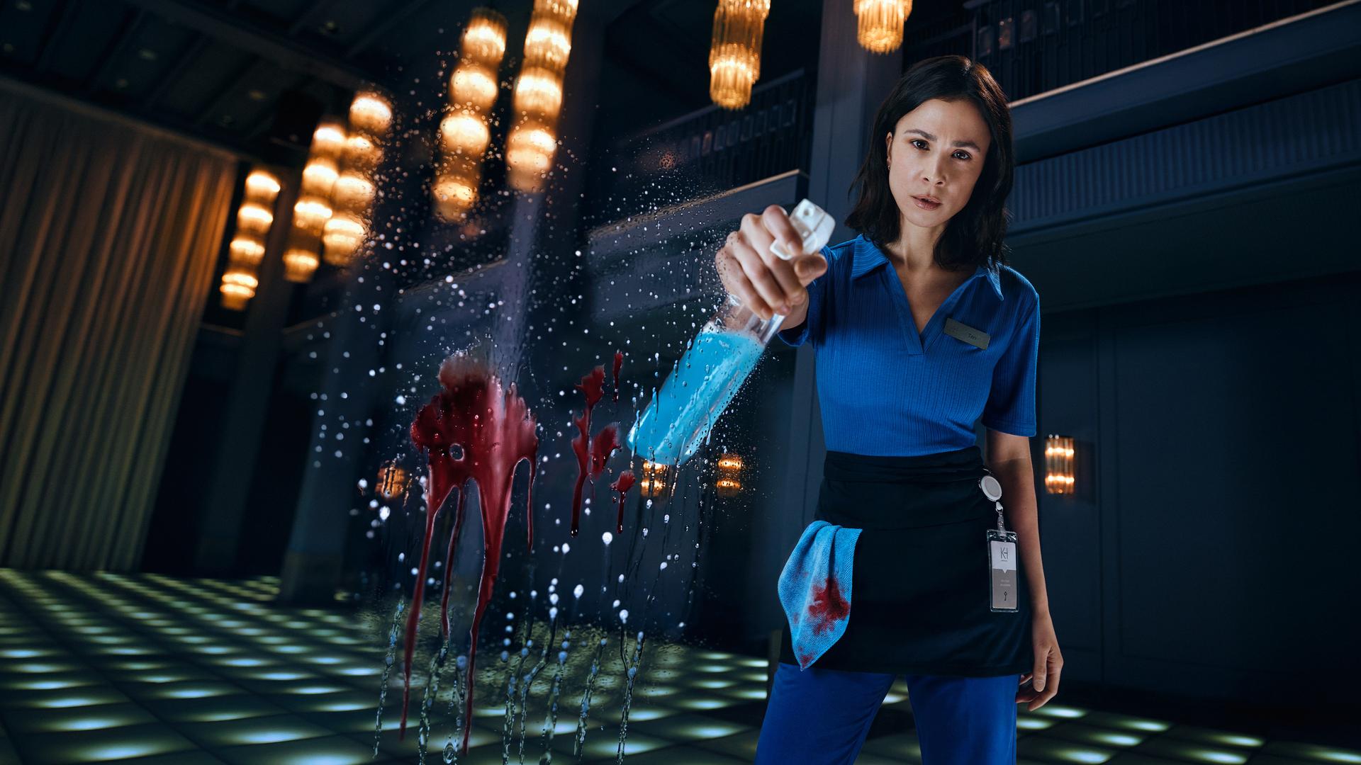 Teri Marquard (Aylin Tezel) steht in Putzkleidung und einer Sprühflasche in der rechten Hand vor der Kamera. Auf der Kameralinse ist ein roter Blutsfleck vermischt mit Putzmittel.