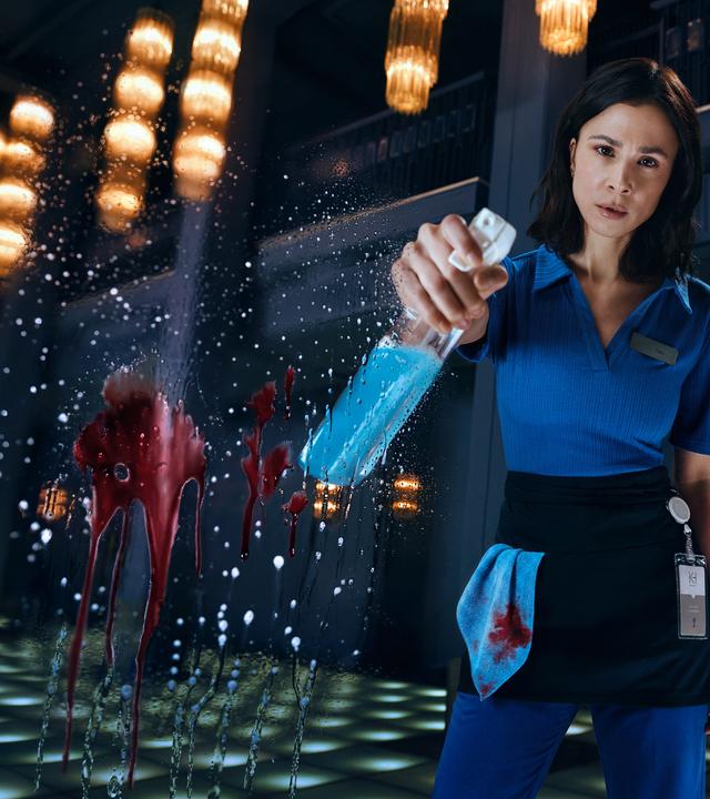 Teri Marquard (Aylin Tezel) steht in Putzkleidung und einer Sprühflasche in der rechten Hand vor der Kamera. Auf der Kameralinse ist ein roter Blutsfleck vermischt mit Putzmittel.
