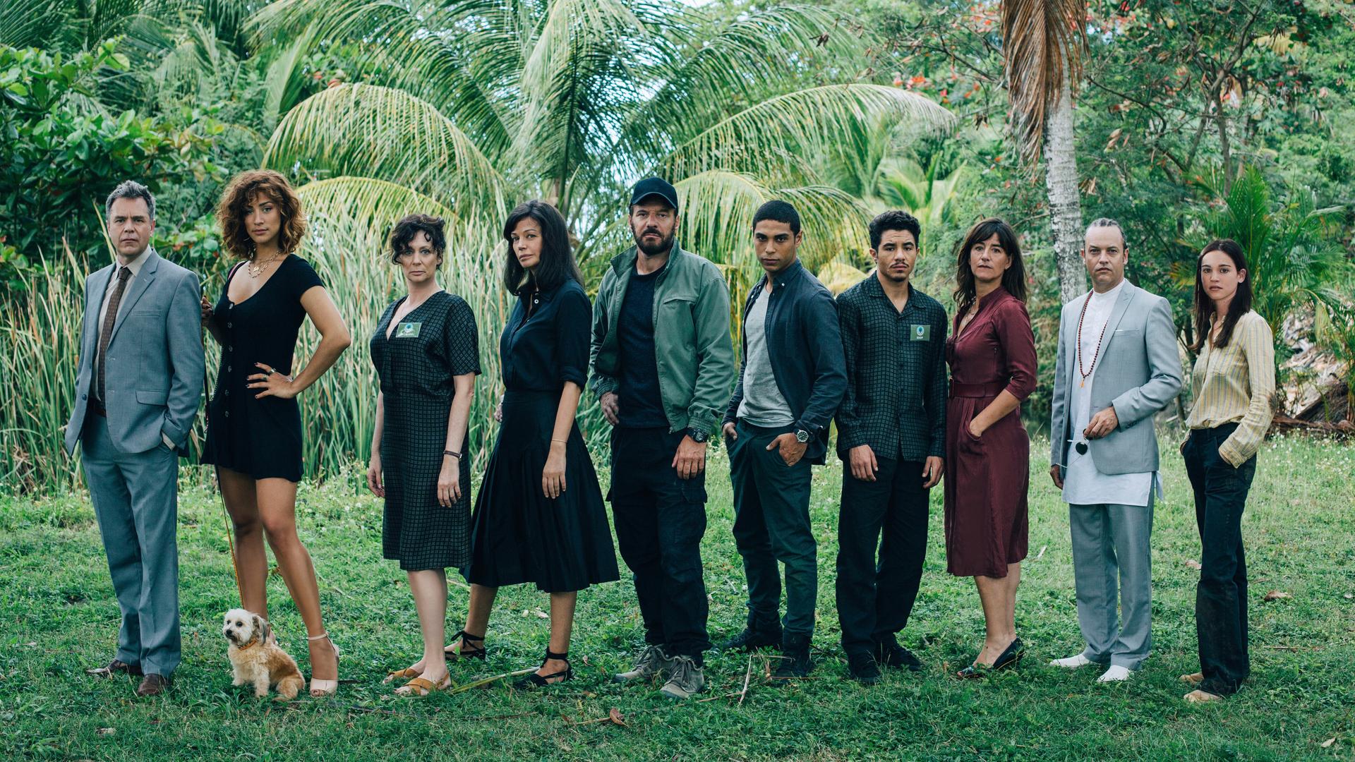 "They Were Ten": Zehn Menschen stehen nebeneinander auf einer Wiese vor Dschungelkulisse mit Palmen: Gilles (Guillaume de Tonquédec), Kelly (Manon Azem mit Hund Bertrand), Myriam (Isabelle Candelier), Eve (Marianne Denicourt), Xavier (Samuel Le Bihan), Malik (Nassim Lyes), Eddy (Samy Seghir), Victoria (Romane Bohringer), Vincent (Patrick Mille) und Nina (Matilda Lutz).