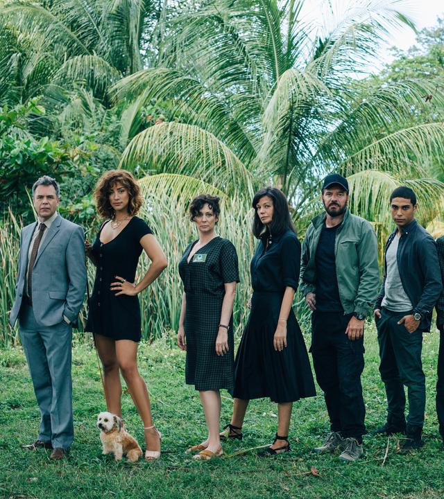 "They Were Ten": Zehn Menschen stehen nebeneinander auf einer Wiese vor Dschungelkulisse mit Palmen: Gilles (Guillaume de Tonquédec), Kelly (Manon Azem mit Hund Bertrand), Myriam (Isabelle Candelier), Eve (Marianne Denicourt), Xavier (Samuel Le Bihan), Malik (Nassim Lyes), Eddy (Samy Seghir), Victoria (Romane Bohringer), Vincent (Patrick Mille) und Nina (Matilda Lutz).