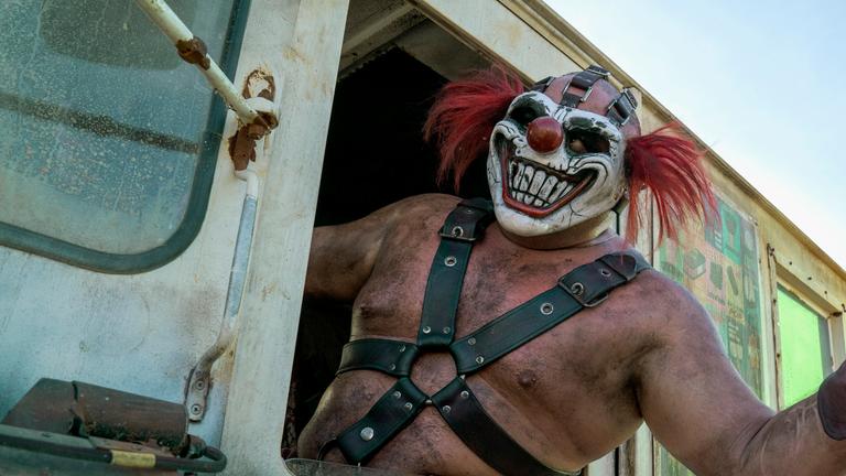 Ein Mann mit furchterregender Clownsmaske (Samoa Joe), genannt Sweet Tooth, lehnt seinen nackten und mit Schmutz verdreckten Oberkörper aus dem Fenster eines fahrenden Autos. Sein Oberkörper ist zusätzlich mit mehreren Gurten aus Leder umschnallt, die in der Mitte des Oberkörpers durch mehrere Ringe zusammengehalten werden. Mit seinem linken Arm deutet er ein Winken an. Das Auto, aus dem er sich lehnt, ist ein heruntergekommener alter Eiswagen.