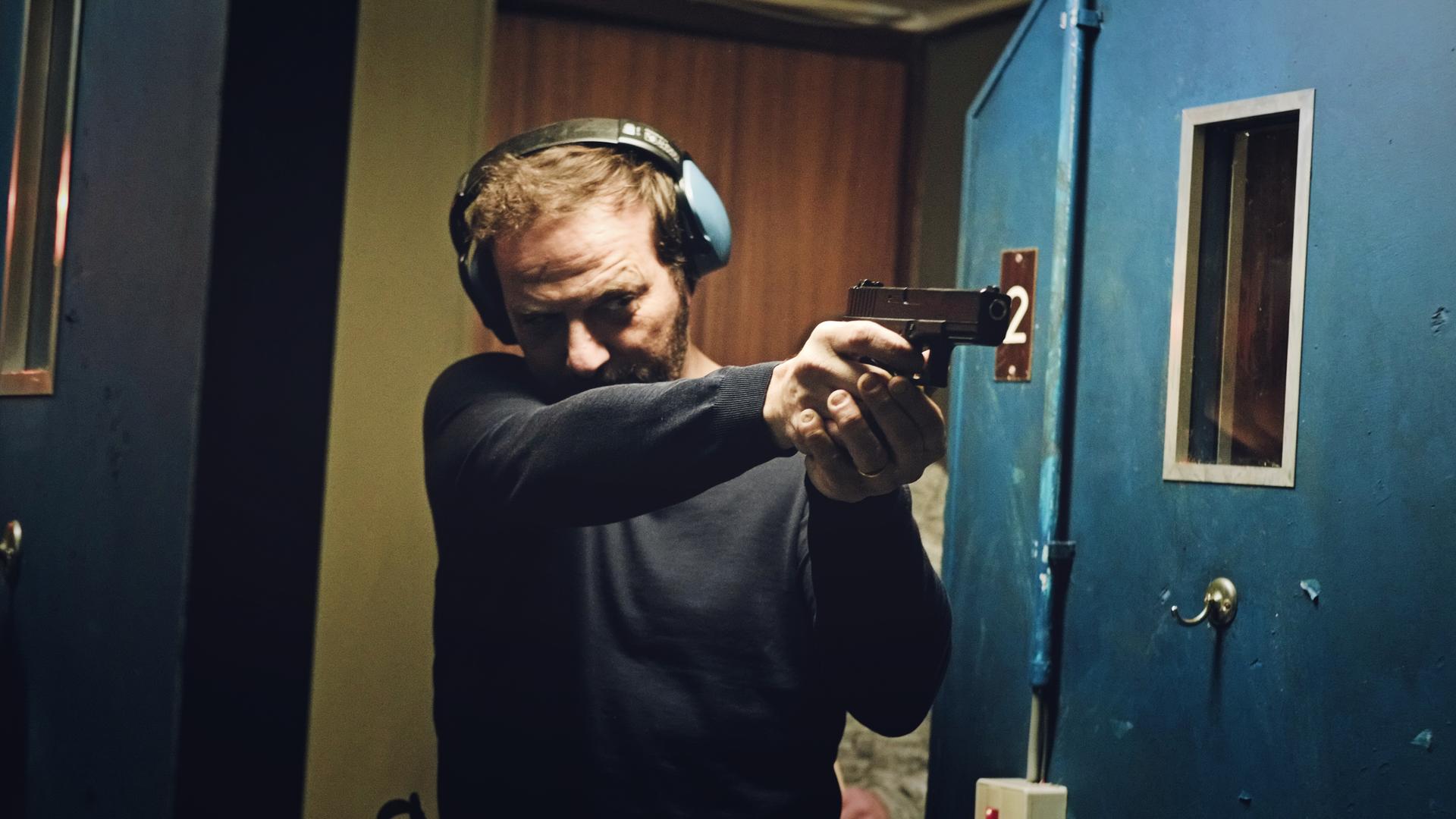 Ein Mann mit schalldichten Kopfhörern richtet eine Waffe geradeaus.