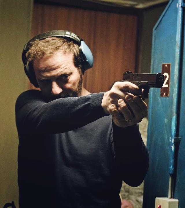 Ein Mann mit schalldichten Kopfhörern richtet eine Waffe geradeaus.