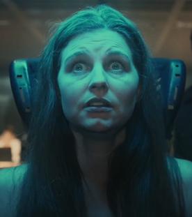 Laurence (Myriem Akheddiou) sitzt mit weit aufgerissenen Augen auf einem Stuhl. Sie sieht verängstigt aus. Um sie herum ist gedämpftes Licht und im Hintergrund steht ein Mann im Anzug, der sich ihr annähert.