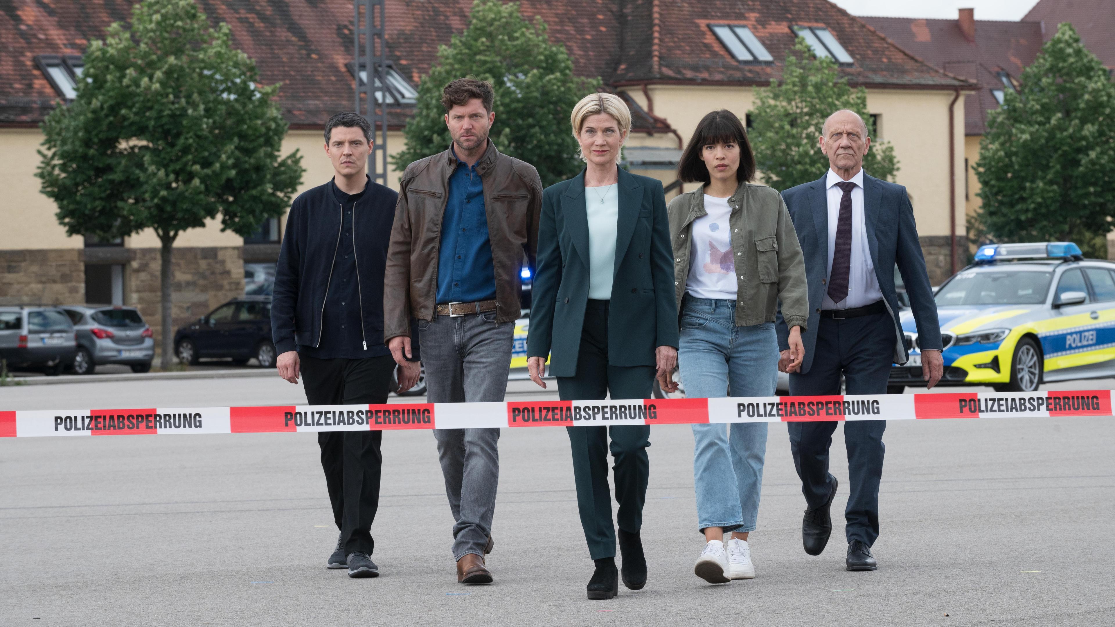 Fünf Männer und Frauen laufen hinter einem Polizeiabsperrungs-Band.