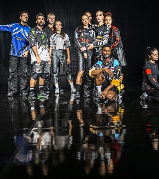 Gruppenbild des ensembles in Sporttrikots. Hinten stehen zwei Vierergruppen. Vor der rechten Gruppe kniet ein Mann und rechts neben dieser Gruppe kniet eine Frau, die zur Seite schaut.