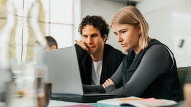 Zwei junge Menschen sitzen in einem hellen Büro konzentriert vor einem Laptop. Gemeinsam betrachten sie den Bildschirm – als Symbolbild für digitale Recherche, Faktencheck und Verifikation beim ZDF.