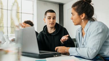 Typical für ZDF Trainee Schwerpunkt Medienrecherche: Zwei Junge Menschen besrepchen sich vor einem Laptop am Schreibtisch sitzend