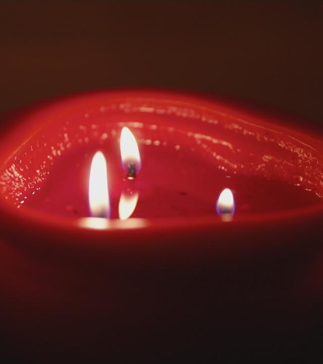 Eine brennende rote Kerze mit drei Dochten.