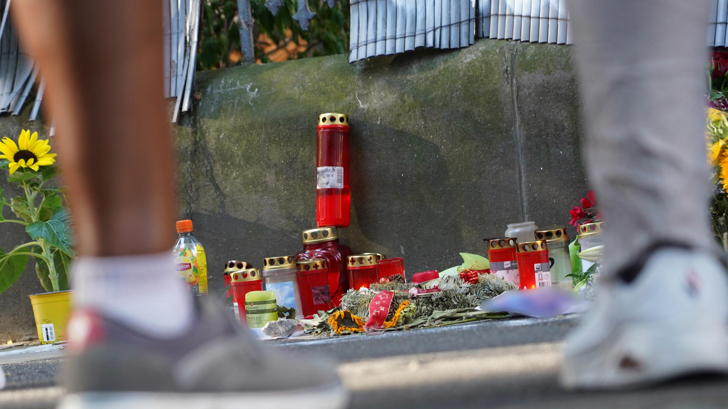 Zwei Menschen stehen vor einem Zaun, an dem mit Kerzen und Blumen eines von der Polizei erschossenen Jugendlichen gedacht wird.