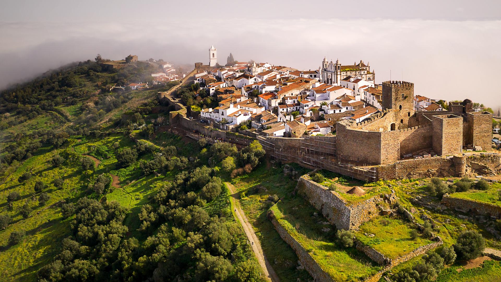 Luftaufnahme: Monsaraz liegt inmitten grüner Wiesen und Wälder im Morgennebel.