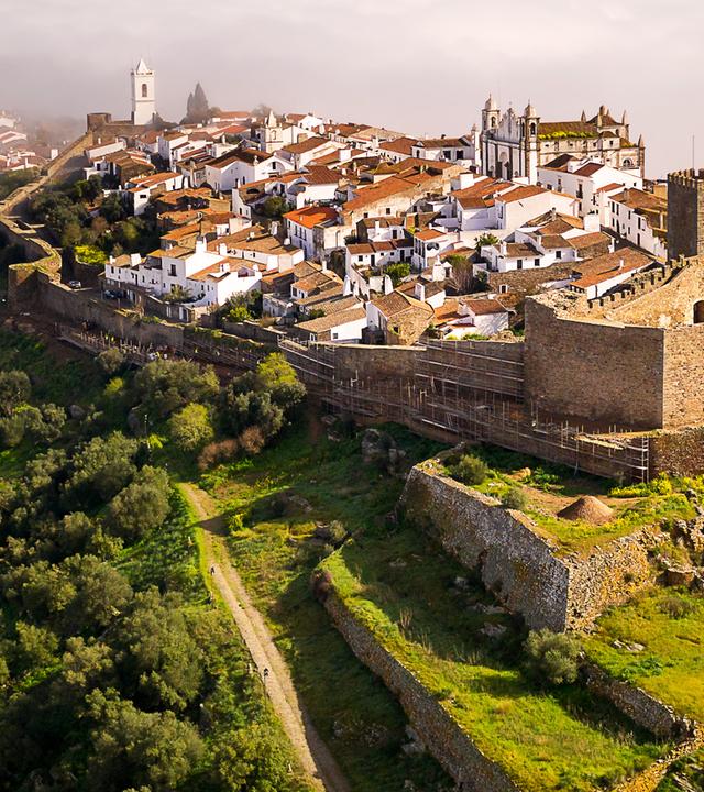 Luftaufnahme: Monsaraz liegt inmitten grüner Wiesen und Wälder im Morgennebel.
