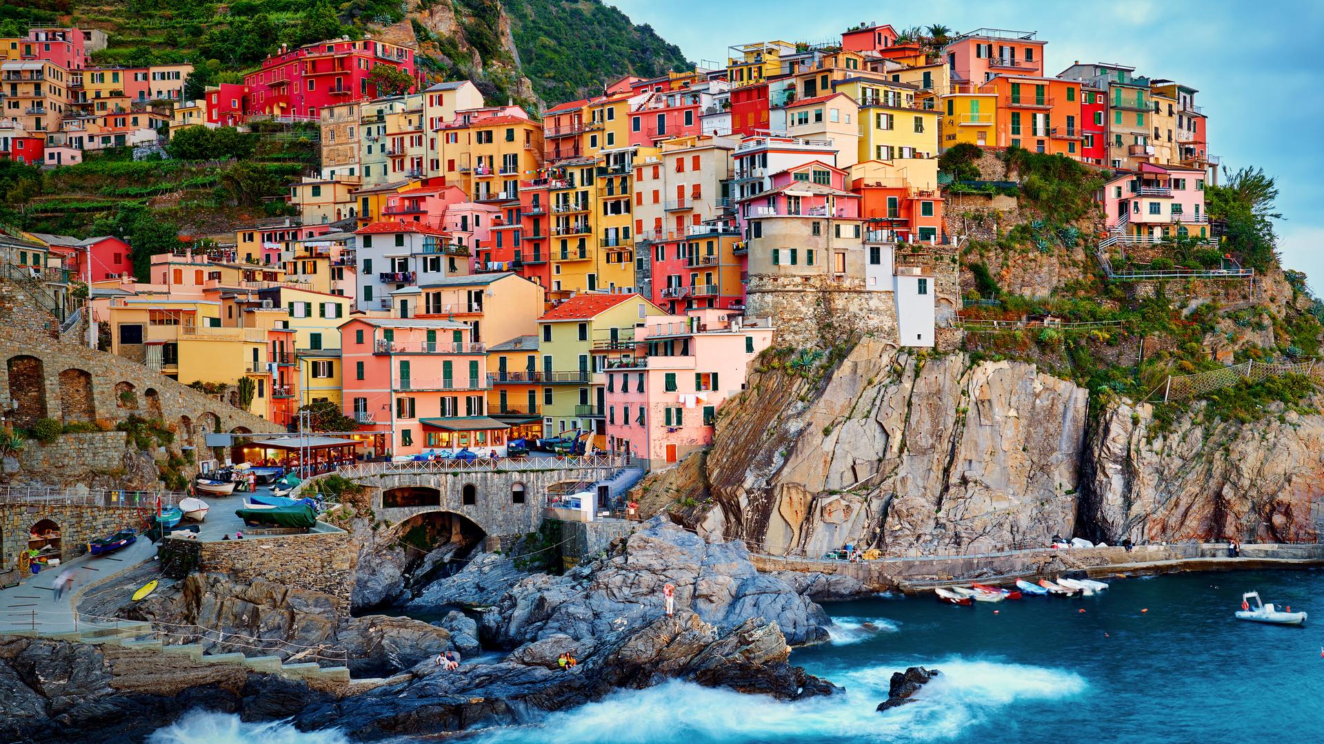 Blick vom Meer aus auf ein Dorf, auf Manarola. Bunte Häuser schmiegen sich an eine steile, felsige Küste.