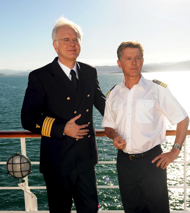 Oskar Schifferle (Harald Schmidt) und Dr. Sander (Nick Wilder) stehen an der Reling des Traumschiffes und schauen zufrieden in die Ferne. 