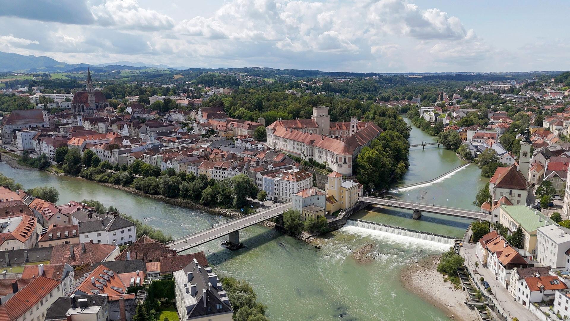 Luftaufnahme von Schloss Lamberg in Steyr, einem imposanten Schloss, das von der historischen „Styraburg“ abstammt und von grünen Wäldern und Feldern umgeben ist.