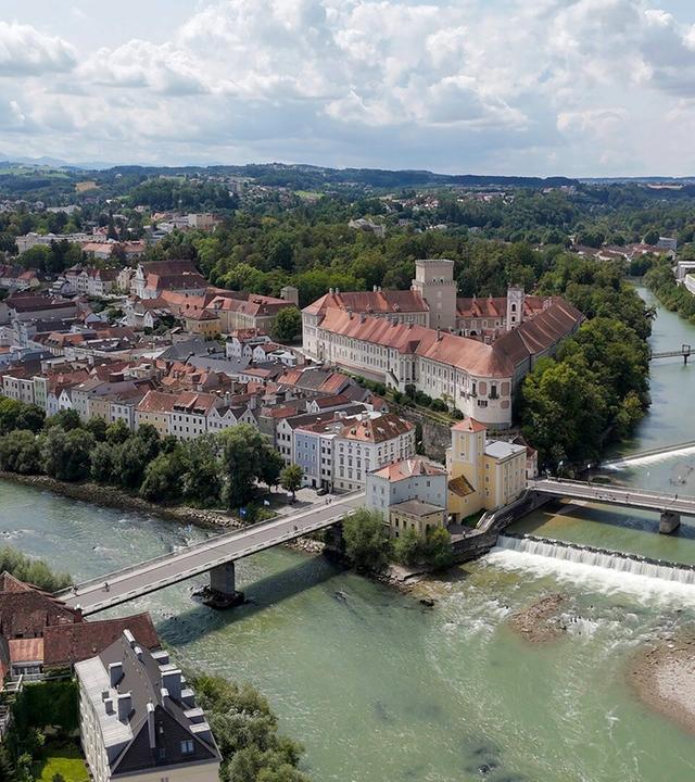 Luftaufnahme von Schloss Lamberg in Steyr, einem imposanten Schloss, das von der historischen „Styraburg“ abstammt und von grünen Wäldern und Feldern umgeben ist.
