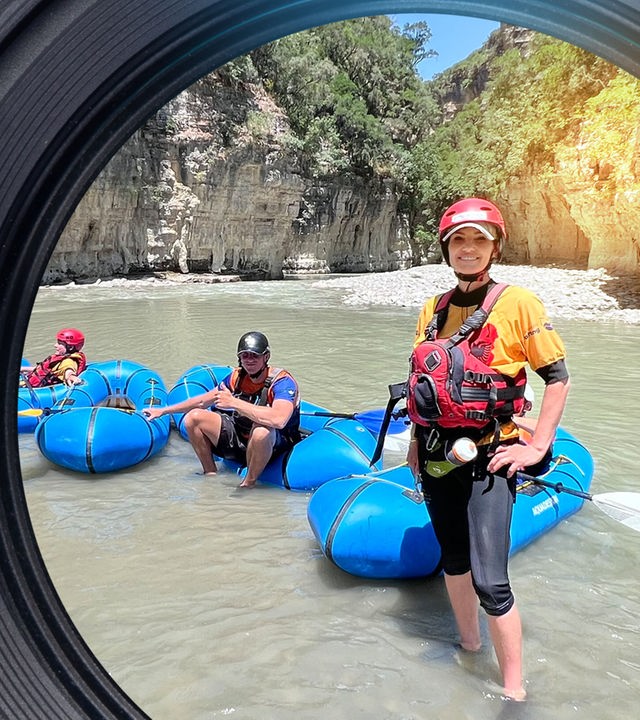 Rafting-Führerin Alma steht im Wasser vor ihrem Boot in einem Canyon. Hinter ihr sind drei Personen in weiteren Booten.