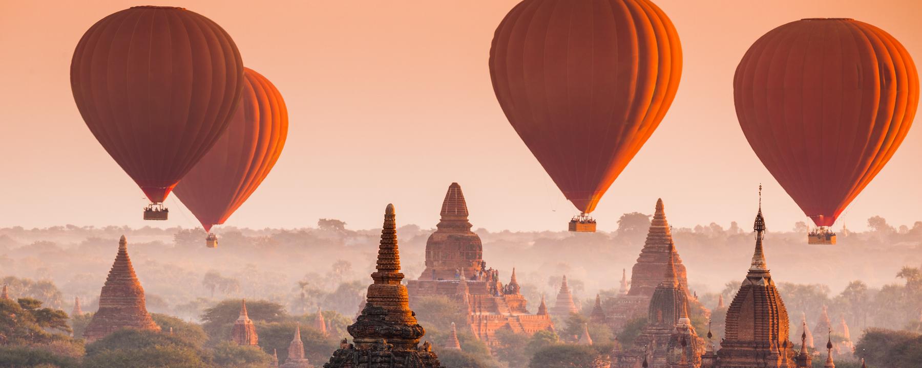 Heißluftballons schweben über Pagoden im Nebel.