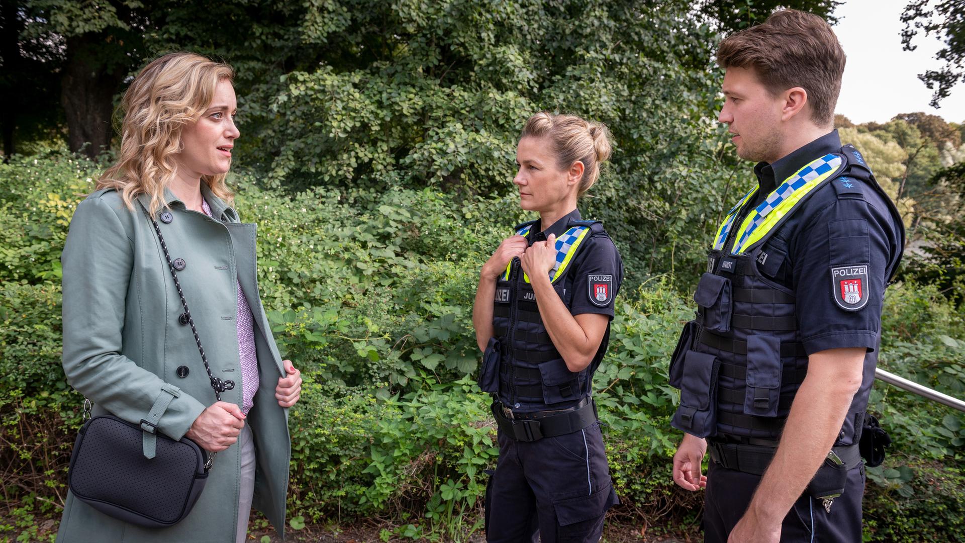 "Notruf Hafenkante - Trennungsschmerzen": Die Polizistin Franzi Jung (Rhea Harder-Vennewald) und ihr Kollege Nick Brandt (Raúl Richter) stehen nebeneinander in einem Park. Vor ihnen steht Anna Palmer (Judith Richter).