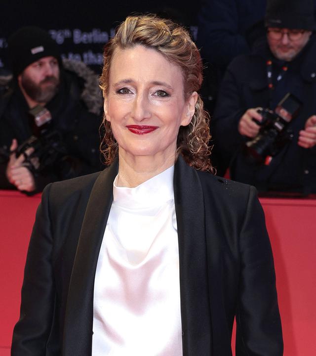 Frau steht auf rotem Teppich und schaut lächelnd in die Kamera.