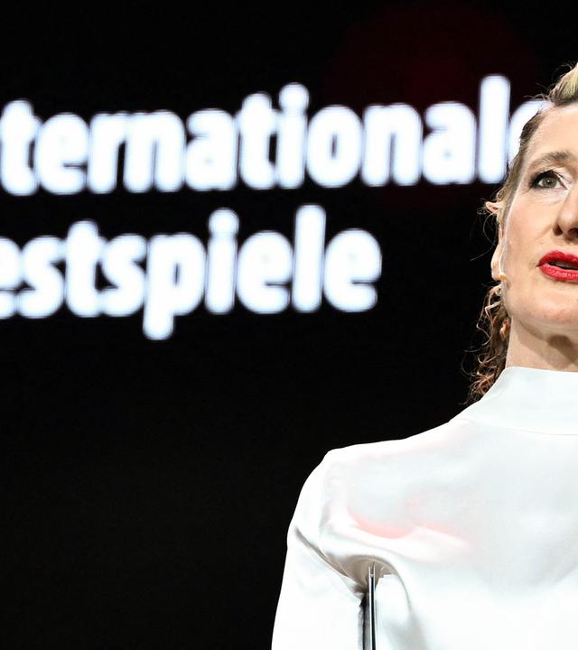 Frau steht auf Bühne und spricht zum Publikum