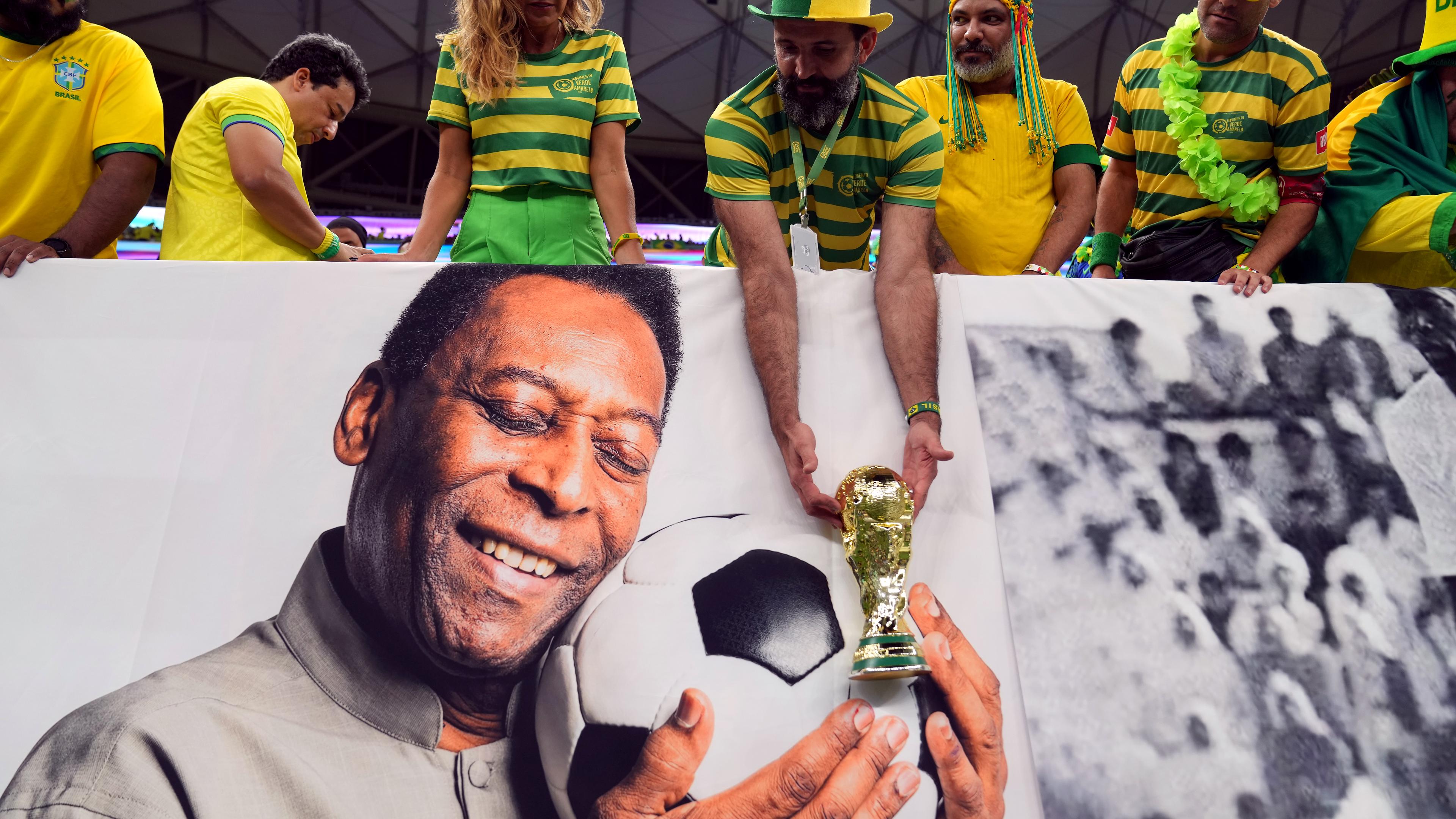 Ein brasilianischer Fan hält vor dem Spiel eine nachgebildete WM-Trophäe über das Bild des ehemaligen Spielers Pelé.