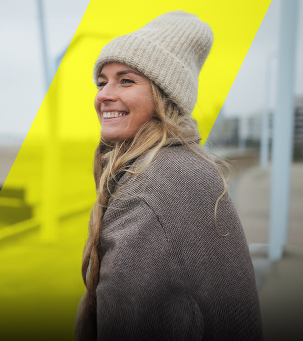 Eine junge Frau lächelt und schaut in die Weite. Im Hintergrund ist ein Strand zu sehen.