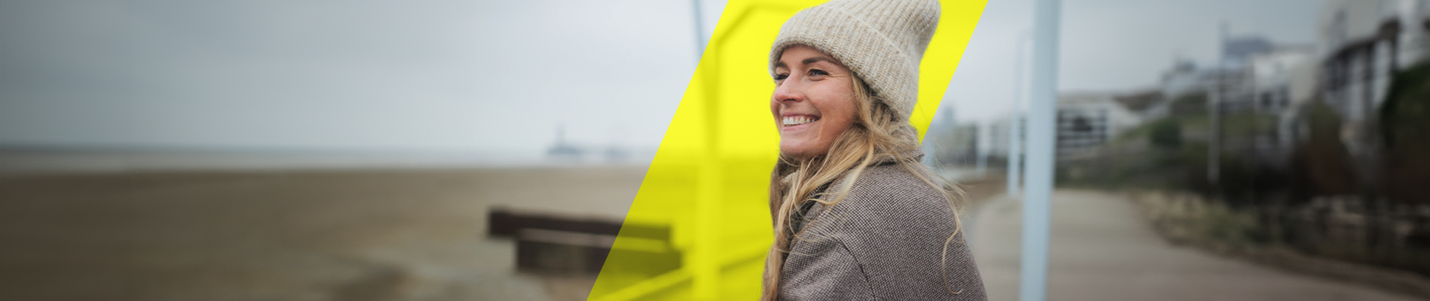 Eine junge Frau lächelt und schaut in die Weite. Im Hintergrund ist ein Strand zu sehen.