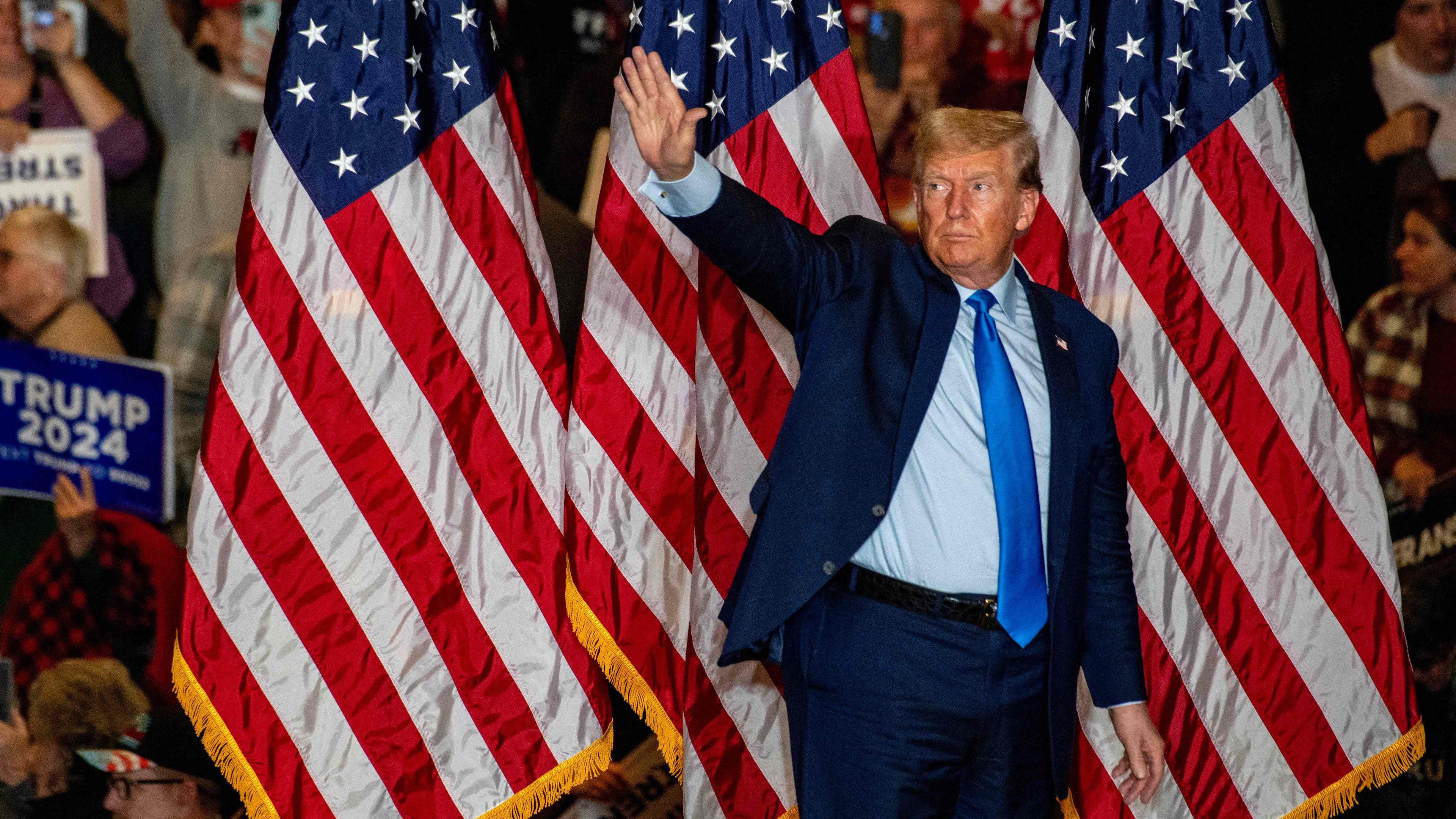 Donald Trump steht bei einer Wahlkampfveranstalgung vor US-Flaggen und winkt in die Menge