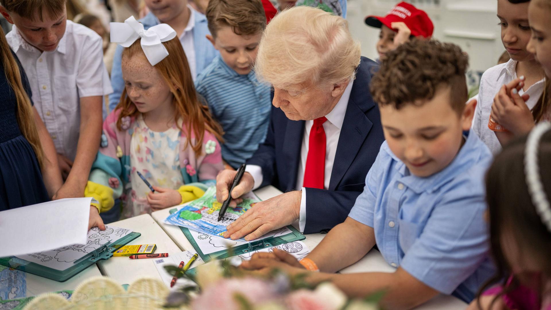 Ein älterer Mann im Anzug malt an einem Tisch, umringt von Kindern.