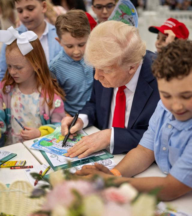 Ein älterer Mann im Anzug malt an einem Tisch, umringt von Kindern.