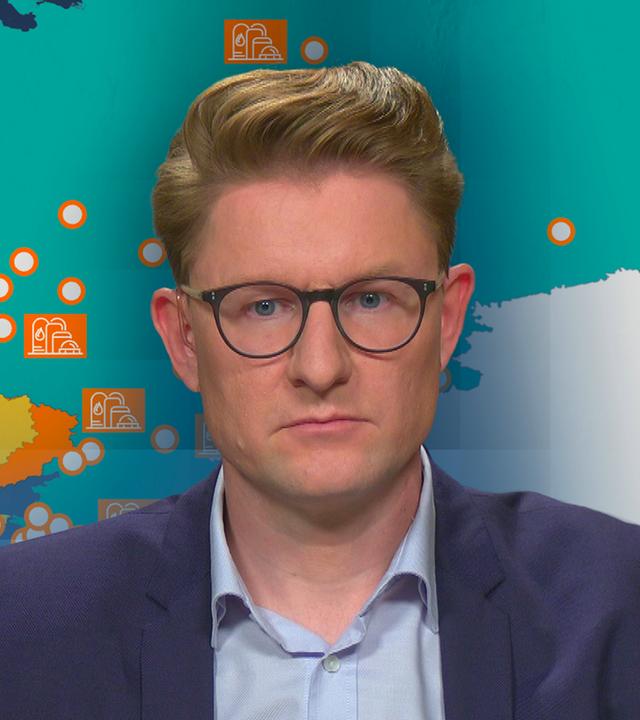 Janis Kluge von der Stiftung Wissenschaft und Politik vor einer Karte Russlands und der Ukraine. Es ist eine Ölraffinerie zu sehen.