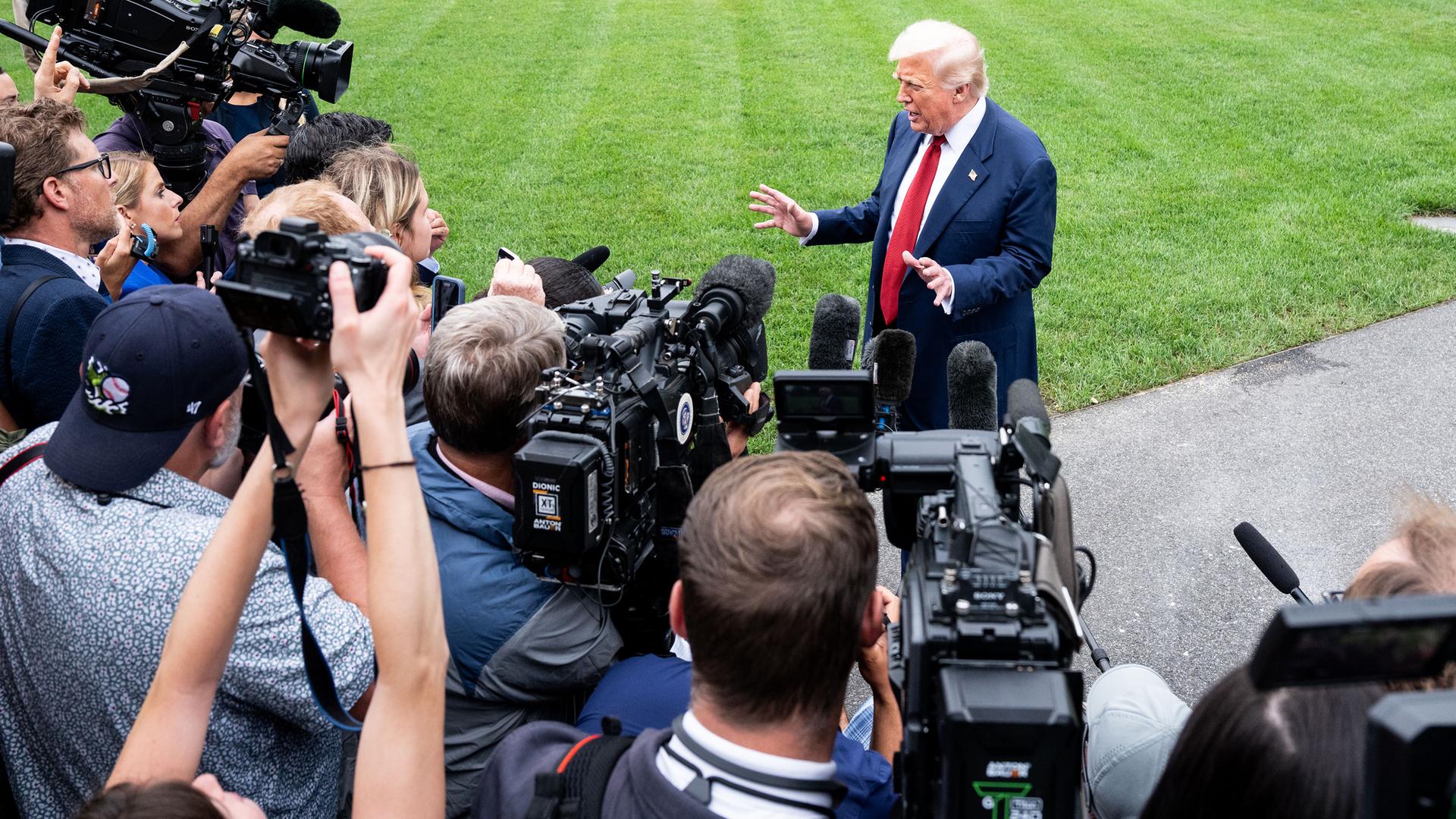 Ein älterer Mann im Anzug steht gestikulierend vor einer Schaar Reporter mit Kameras und Mikros.