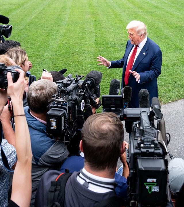 Ein älterer Mann im Anzug steht gestikulierend vor einer Schaar Reporter mit Kameras und Mikros.