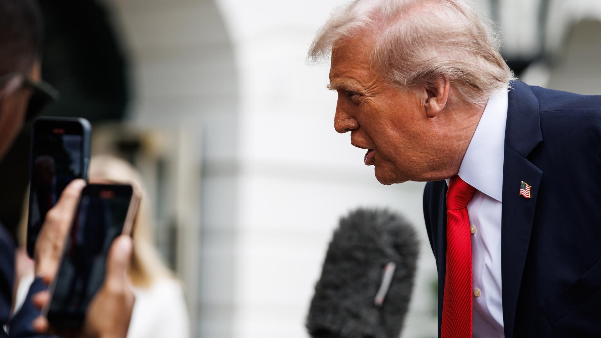 Ein älterer Mann im Anzug beugt sich vor und spricht in Handy-Kameras und Mikros, die ihm entgegen gehalten werden.