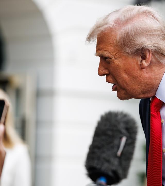 Ein älterer Mann im Anzug beugt sich vor und spricht in Handy-Kameras und Mikros, die ihm entgegen gehalten werden.