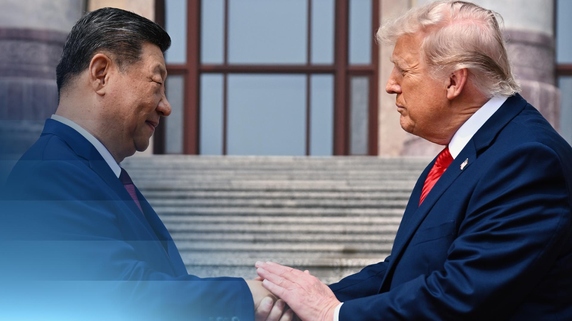 Das Seitenprofil von Trump und Xi. Sie stehen sich gegenüber. Xi lächelt leicht, Trump guckt eher ernst. Sie tragen beide einen blauen Anzug und schütteln sich die Hand.