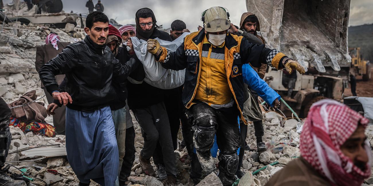 Männer tragen einen Plasticksack aus den Trümmern des Erdbebens