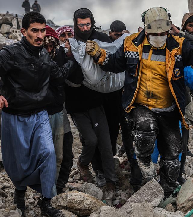 Männer tragen einen Plasticksack aus den Trümmern des Erdbebens