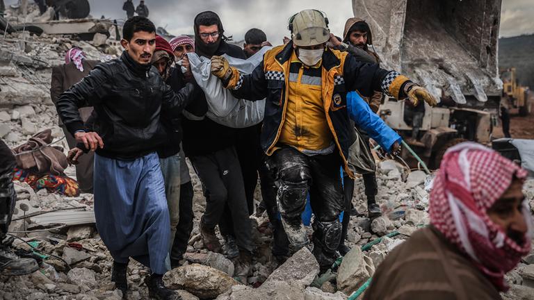 Männer tragen einen Plasticksack aus den Trümmern des Erdbebens