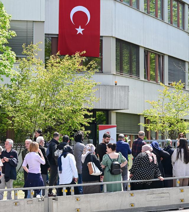 Eine Schlange an Menschen, im Hintergrund eine türkische Flagge